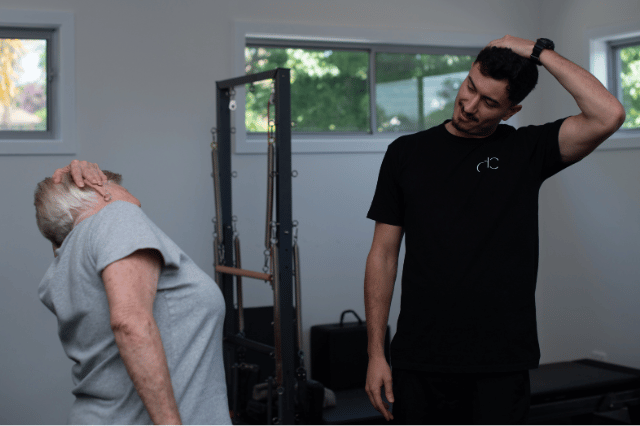 Older woman and physiotherapist performing neck stretches together in a fitness studio.