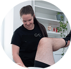 Person in black shirt assisting another person's leg in a therapy or clinical setting.