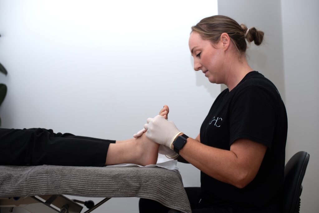 A healthcare worker examines a patient's foot on a treatment table in a clinical setting.