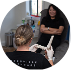 A healthcare worker shows a foot model to a seated patient in a clinic room.