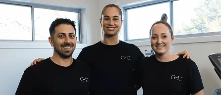 Three people standing side by side indoors, all wearing matching black t-shirts and smiling.