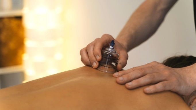Person receiving cupping therapy on their back with a clear cup applied by a practitioner's hands.