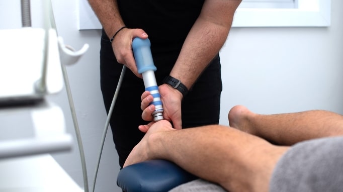 A person uses a handheld device on another person's bare foot in a clinical setting.