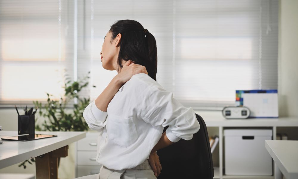Person at desk holding neck and back, showing pain—possibly seeking plantar fasciitis treatment.